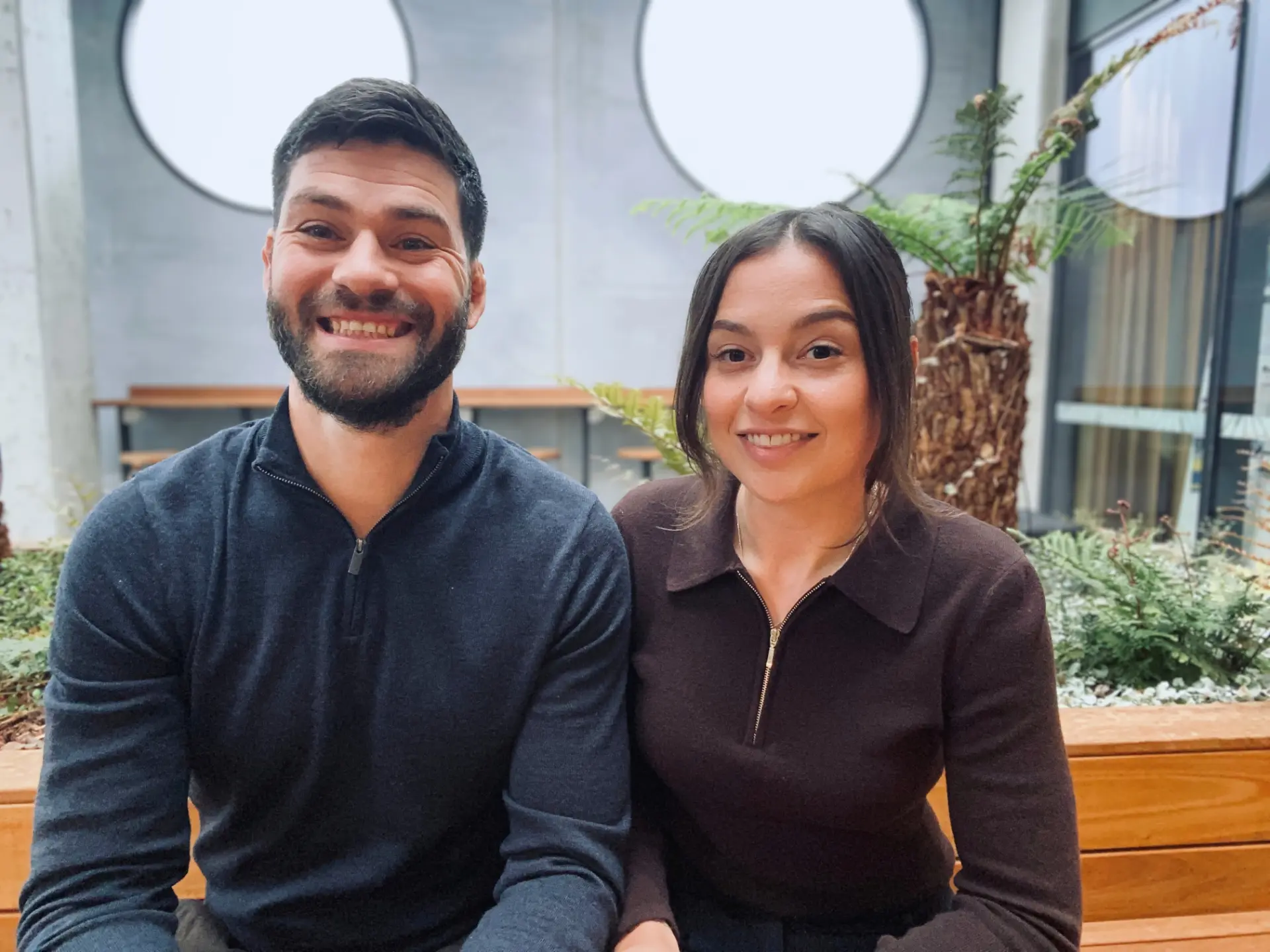 Travis and Madi, the husband-and-wife team behind Stronghold, sitting side by side and smiling in a leafy courtyard.